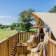 Wooden deck of the Papillon safari tent overlooking a grassy field, blue sky, and relaxing seating area.