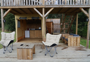 Zona exterior del safari tent Papillon en Domaine Bonneblond, Francia, con terraza y muebles de madera.