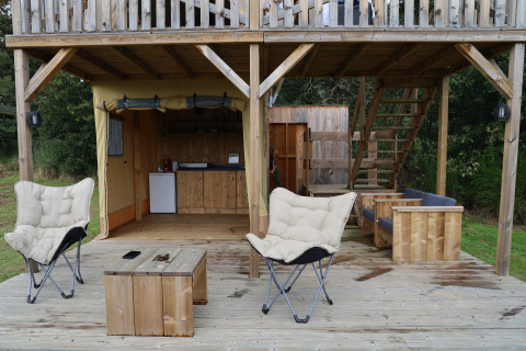 Outdoor lounge area at the Papillon safari tent in Domaine Bonneblond, France, featuring wooden furniture.