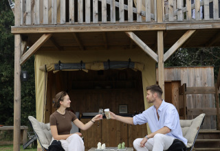 Two people toast in front of the Papillon safari tent at Domaine Bonneblond in France, surrounded by nature.