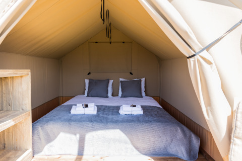 Interior de la tienda safari Papillon en Domaine Bonneblond, Francia, con cama doble y toallas dobladas.