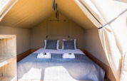 Interior de la tienda safari Papillon en Domaine Bonneblond, Francia, con cama doble y toallas dobladas.