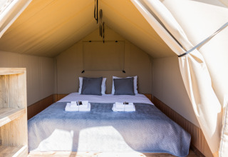 Interior de la tienda safari Papillon en Domaine Bonneblond, Francia, con cama doble y toallas dobladas.