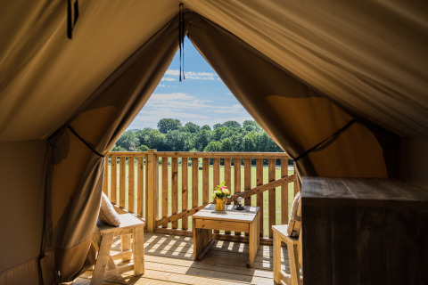 View from the Papillon safari tent at Domaine Bonneblond, France, featuring a wooden deck and scenic fields.
