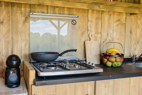 Cocina exterior en la tienda safari Papillon de Domaine Bonneblond, Francia, con estufa de gas y cesta de frutas.