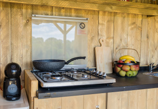 Cocina exterior en la tienda safari Papillon de Domaine Bonneblond, Francia, con estufa de gas y cesta de frutas.