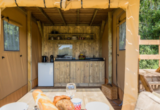 Køkken i safaritelten Papillon på Domaine Bonneblond i Frankrig, med træ bord, køleskab og service.