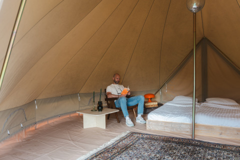 Binnen in een Bell tent op Domaine Bonneblond in Frankrijk leest een man een boek naast een opgemaakt bed.