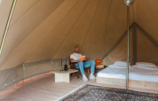 Binnen in een Bell tent op Domaine Bonneblond in Frankrijk leest een man een boek naast een opgemaakt bed.