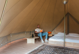 Binnen in een Bell tent op Domaine Bonneblond in Frankrijk leest een man een boek naast een opgemaakt bed.