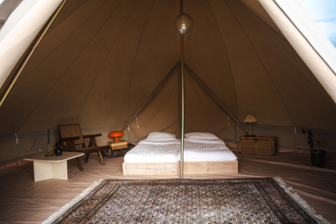 Interior of a Bell tent at Domaine Bonneblond in France, featuring twin beds, vintage chairs and a rug.