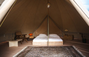 Interior of a Bell tent at Domaine Bonneblond in France, featuring twin beds, vintage chairs and a rug.