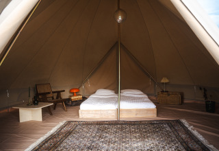 Interior of a Bell tent at Domaine Bonneblond in France, featuring twin beds, vintage chairs and a rug.