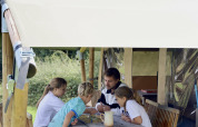 Family playing a board game at a wooden table outside a safari tent with private facilities in France.