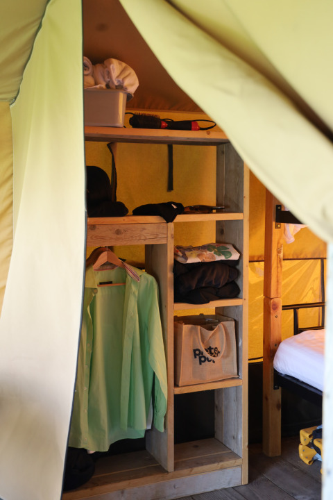 Interior of a safari tent at Domaine Bonneblond in France, showing storage shelves and hanging clothes.