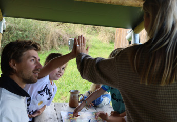 Family plays a board game together at a wooden table in a safari tent at Domaine Bonneblond, France.