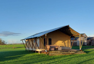 Safari tent Glampingtent Jannie at Glamping Franse Peer in the Netherlands set on a green field under blue sky.
