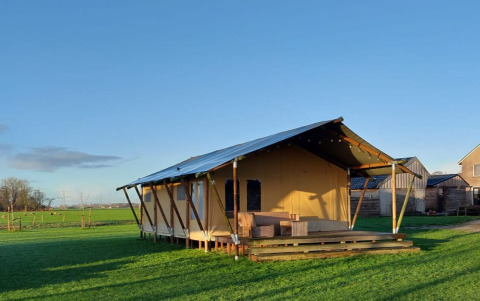 Safaritent Glampingtent Jannie bij Glamping Franse Peer in Nederland op een groen veld onder blauwe hemel.