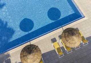 Luchtfoto van zwembad met blauw water, gele ligbedden en rieten parasols bij Flower Camping La Davière Plage.