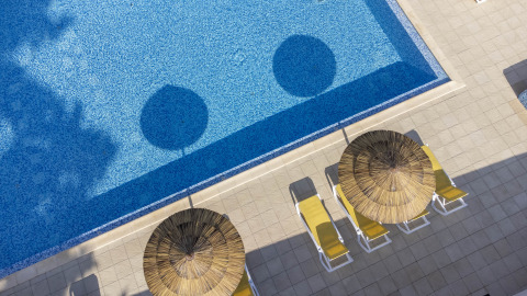 Luchtfoto van zwembad met blauw water, gele ligbedden en rieten parasols bij Flower Camping La Davière Plage.