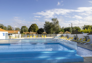Outdoor swimming pool with sun loungers and straw umbrellas at Flower Camping La Davière Plage, France.