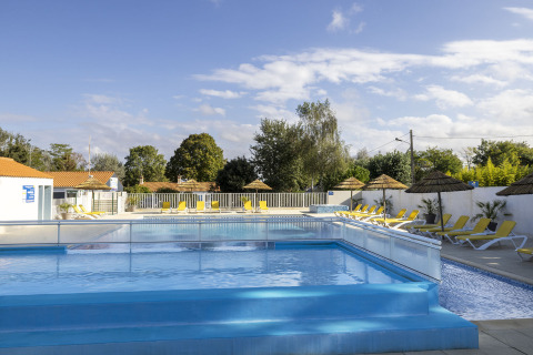 Outdoor swimming pool with sun loungers and straw umbrellas at Flower Camping La Davière Plage, France.