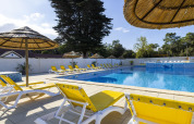 Piscina all'aperto con lettini gialli e ombrelloni in paglia presso il Flower Camping La Davière Plage, Francia.