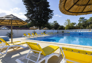 Piscina all'aperto con lettini gialli e ombrelloni in paglia presso il Flower Camping La Davière Plage, Francia.