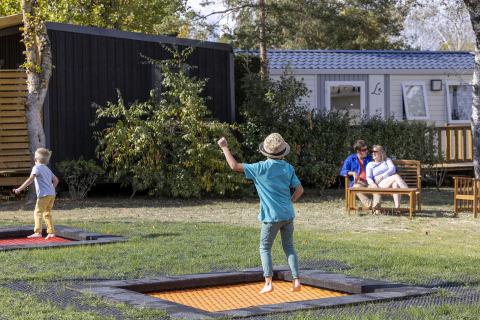 Dos niños juegan en camas elásticas y dos adultos descansan en un banco en Flower Camping La Davière Plage.