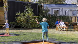 Dos niños juegan en camas elásticas y dos adultos descansan en un banco en Flower Camping La Davière Plage.