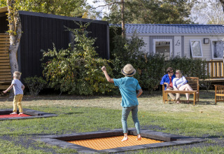 Dos niños juegan en camas elásticas y dos adultos descansan en un banco en Flower Camping La Davière Plage.