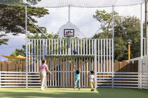 Niños juegan baloncesto en una cancha al aire libre con red de seguridad en Flower Camping La Davière Plage, Francia.