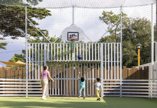 Bambini giocano a basket su un campo all'aperto protetto da rete al Flower Camping La Davière Plage in Francia.