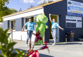 Twee medewerkers en een groene mascotte heten gasten welkom bij Flower Camping La Davière Plage in Pays de la Loire.