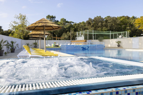 Piscina all’aperto con vasca idromassaggio, lettini gialli e ombrelloni in paglia al Flower Camping La Davière Plage.