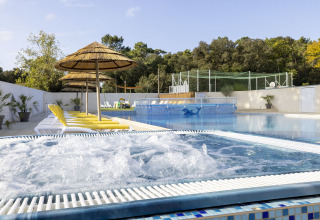 Outdoor pool with hot tub, yellow loungers, and straw umbrellas at Flower Camping La Davière Plage, France.