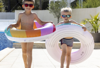 Twee kinderen met zonnebril en zwemband lopen bij het zwembad op Flower Camping La Davière Plage in Frankrijk.