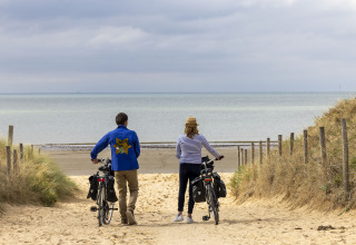 Due persone camminano con le biciclette verso la spiaggia al Flower Camping La Davière Plage in Pays de la Loire, Francia.