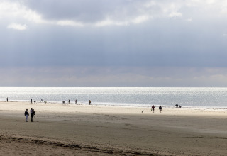 Menschen spazieren am Strand bei Flower Camping La Davière Plage, Pays de la Loire, mit bewölktem Himmel.