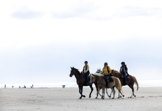 Drie mensen te paard langs het strand bij Flower Camping La Davière Plage in Pays de la Loire, Frankrijk.