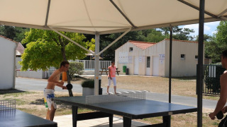 Dos personas juegan al tenis de mesa al aire libre bajo una carpa en Flower Camping La Davière Plage, Francia.