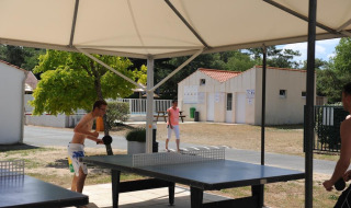 Dos personas juegan al tenis de mesa al aire libre bajo una carpa en Flower Camping La Davière Plage, Francia.