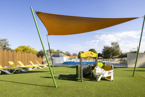 Speelruimte met zonnescherm, ligstoelen en speeltuin bij het zwembad op Flower Camping La Davière Plage.
