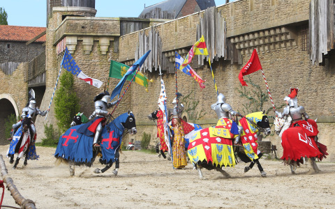 Des chevaliers en armure participent à un tournoi médiéval avec des drapeaux colorés près d’un château en Pays de la Loire, France.