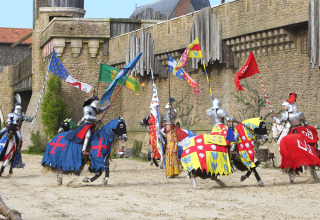 Des chevaliers en armure participent à un tournoi médiéval avec des drapeaux colorés près d’un château en Pays de la Loire, France.