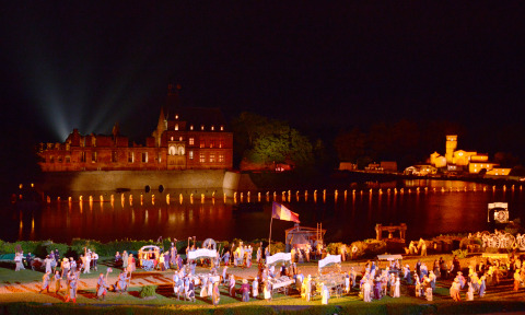 Veduta notturna di un castello illuminato vicino a un lago con spettacolo esterno a Flower Camping La Davière Plage.