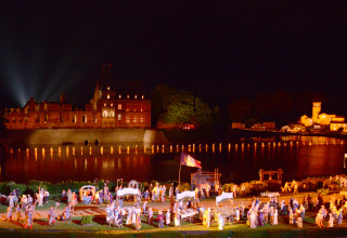 Vue nocturne d’un château illuminé près d’un lac lors d’un spectacle au Flower Camping La Davière Plage, France.