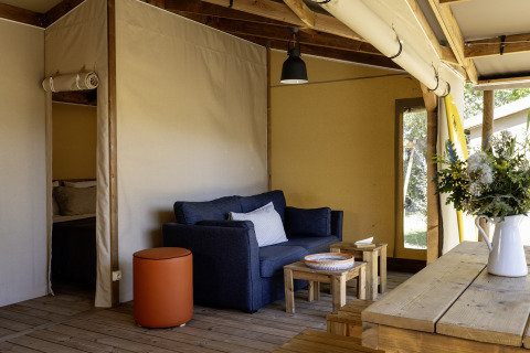Woonruimte in safari tent Hut Cotton Confort met zetel, houten meubilair en bloemen op de tafel.