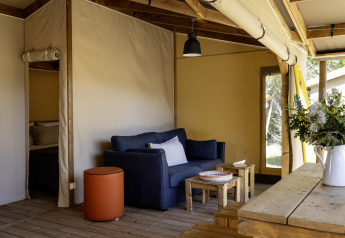 Stueområde i safari teltet Hut Cotton Confort med sofa, træmøbler og blomster i kande på bordet.