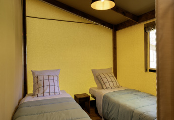 Twee aparte bedden met geruite kussens in een gezellige ruimte van safari tent Hut Cotton Confort.